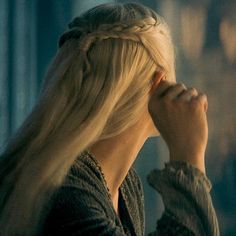 a woman with long blonde hair and braids on her head is looking out the window