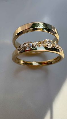 two gold rings with different colored diamonds on top of each other, sitting on a white surface