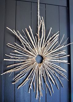 a wreath made out of sticks hanging from the side of a blue door with rope