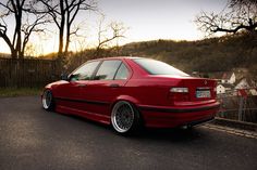 a red car parked on the side of a road next to a fence and trees