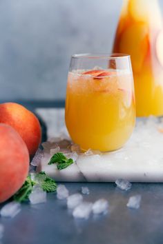 two glasses filled with orange juice on top of ice next to peaches and mint