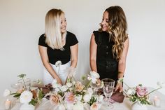 two women standing next to each other at a table with flowers and candles on it