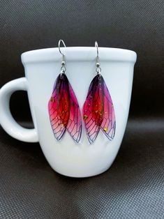 Our enchanting Double Fairy Wing Resin Earrings feature delicately designed fairy wings, beautifully encapsulated in a high-quality resin. With not one, but two wings per earring, these whimsical accessories will transport you to a realm of fantasy and wonder. Available in a stunning range of 9 colors, you can choose the hue that best resonates with your unique style and personality. Indulge in the enchantment and beauty of our lightweight Double Fairy Wing Resin Earrings and let your imagination take flight. To see other jewelry and gifts in our shop, please click this link; https://lacostaskreations.etsy.com Fairy-themed Drop Earrings For Gifts, Fairy Style Drop Earrings For Gifts, Handmade Fairy Drop Earrings, Handmade Fairy Style Drop Earrings, Fairy Style Dangle Earrings For Parties, Fairy Style Drop Earrings, Fairycore Ear Wire Earrings As Gift, Fairycore Butterfly Earrings For Gift, Fairy Grunge Dangle Earrings Gift