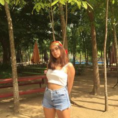 a woman standing in front of trees wearing shorts and a bandana on her head