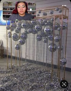 a woman with red hair standing in front of a sculpture made out of silver balls