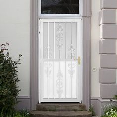 a cat sitting in front of a door on the side of a house with flowers