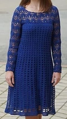 a woman wearing a blue crochet dress standing in front of a brick sidewalk