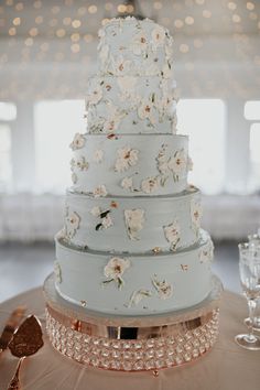 a wedding cake with white flowers on it sitting on a table next to wine glasses