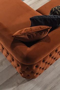 an orange couch with two pillows on it's back and one black pillow sitting on top of it