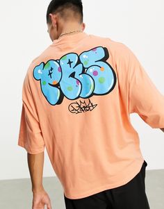 a man wearing an orange shirt with graffiti on it's back and his hand in his pocket