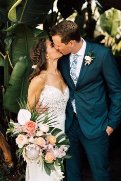 a bride and groom kissing each other in front of some tropical plants at their wedding