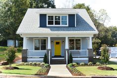 a blue and white house with a yellow door in the front yard on a sunny day