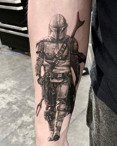 a man with a star wars tattoo on his arm holding a knife and wearing a boba fett helmet