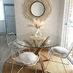 a glass table with chairs around it in front of a window and a round mirror on the wall