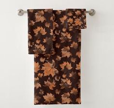 an orange and brown leaf print towel hanging from a metal hook on a white wall