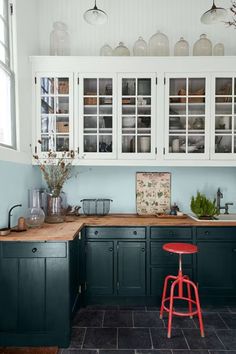 An eclectic kitchen with dark blue counters, white cabinets, a red stool, and various kitchen utensils. Blue Kitchen White Cabinets, Dark Blue Kitchen Walls, Blue And Red Kitchen, Vintage Eclectic Kitchen, Green Blue Kitchen, Vintage Paint Colors, Dark Blue Kitchen, Red Stool, Red Kitchen Cabinets