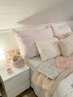 a white bed topped with lots of pillows next to a night stand and table lamp