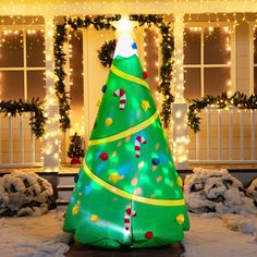 a large inflatable christmas tree sitting on top of snow covered ground next to a house