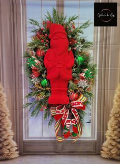 a christmas wreath with a red teddy bear hanging from it's side in front of a door