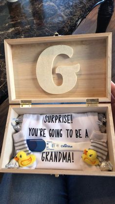 someone is holding up a wooden box with the letter g in it that says surprise you're going to be a grandma