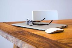 a laptop computer sitting on top of a wooden table next to a pair of glasses