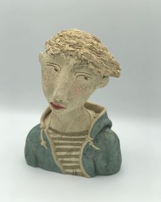 a ceramic figurine of a woman's head wearing a blue jacket and striped shirt