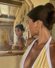 a woman looking at herself in the mirror with her hair pulled back and wearing gold hoop earrings