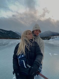 two people are standing on the ice with skis in their hands and one is holding onto another person's shoulder