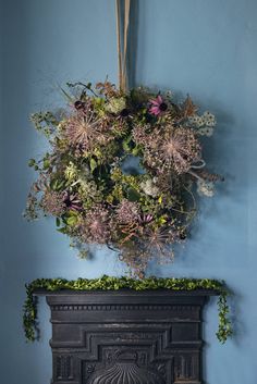 an image of a wreath hanging on the wall above a fire place with flowers in it