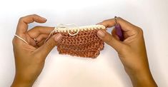 two hands are holding up a piece of crocheted material that is brown and white