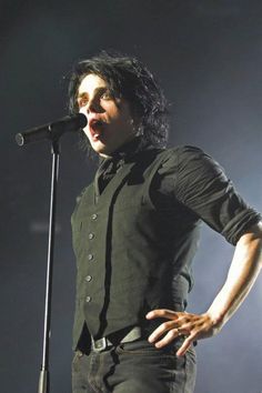 a man standing in front of a microphone with his hands on his hips while singing