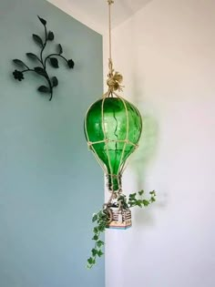 a green glass lantern hanging from a hook on a wall next to a potted plant