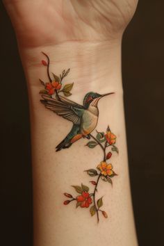 a hummingbird on a branch with flowers and leaves around it's wrist tattoo