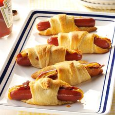 four hot dogs wrapped in crescented bread on a white platter with ketchup