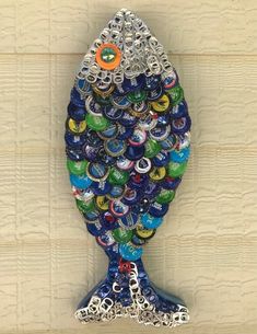 a bottle cap fish made out of beer caps on a wooden wall with chains hanging from it's sides