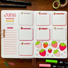 an open planner with strawberries on it next to some pens and pencils, along with other office supplies