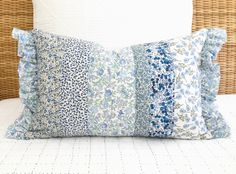 a close up of a pillow on a bed with white sheets and blue floral pillows