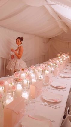 a woman standing next to a long table filled with white plates and pink napkins