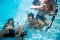 two men and a woman in the water with fishing rods on their feet, holding poles