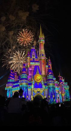 the castle is lit up at night with colorful lights and fireworks in the sky above it