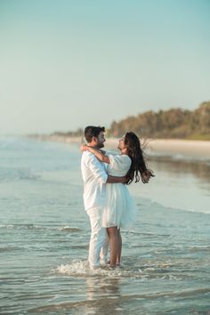 a man and woman are standing in the water at the beach, holding each other