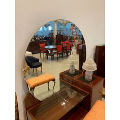 a round mirror sitting on top of a wooden table next to a chair and ottoman