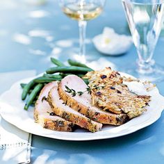 a white plate topped with meat and veggies next to two glasses of wine