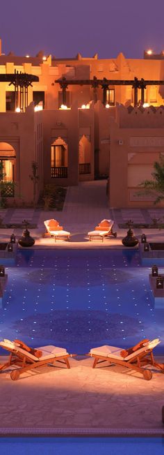 an outdoor swimming pool with chaise lounges in front of the hotel at night