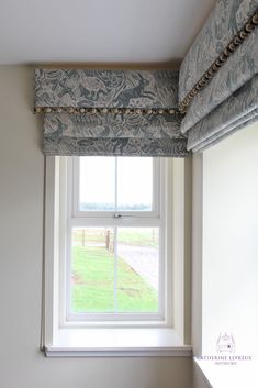 an open window in a white room with blue and green roman shades on the windowsill