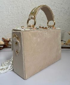 Introducing the Danika Flap Bag, a stunning fusion of bridal elegance and Indian craftsmanship. Hand-beaded with luxurious velvet in enchanting hues of mint, white, and peach, with a beautiful pearl motif, this bag embodies opulence and tradition. Its intricate design, coupled with delicate white suede accents, makes it a standout accessory for brides and lovers of Indian fashion alike. Whether for a wedding ceremony or a cultural celebration, the Danika Flap Bag adds a touch of regal charm to a Cream Rectangular Box Bag For Evening, Cream Rectangular Evening Box Bag, Traditional Evening Shoulder Bag With Pearl Handle, Embellished Beige Evening Bag As Gift, Beige Embellished Evening Bag As Gift, Luxury Cream Shoulder Bag For Party, Cream Embellished Rectangular Clutch, Embellished Cream Rectangular Clutch, Luxury Clutch With Pearl Embroidery For Reception