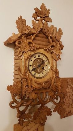 an ornate wooden clock with carved figures on the front and sides, hanging from a wall