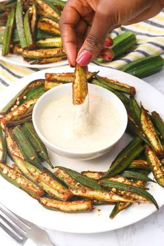 a person dipping some food into a bowl on top of a white plate with green beans