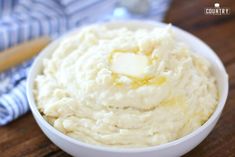 a white bowl filled with mashed potatoes on top of a wooden table next to a blue and white napkin