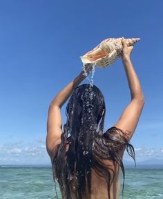 a woman standing in the water with her hands up to her head and holding an object above her head